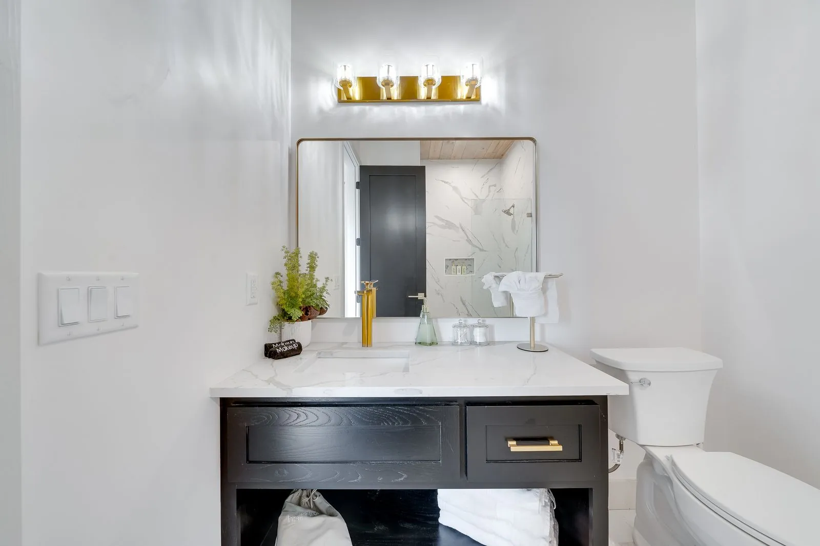 Luxury walk-in shower at The Malibu with marble tile walls, gold rainfall showerhead, and glass enclosure