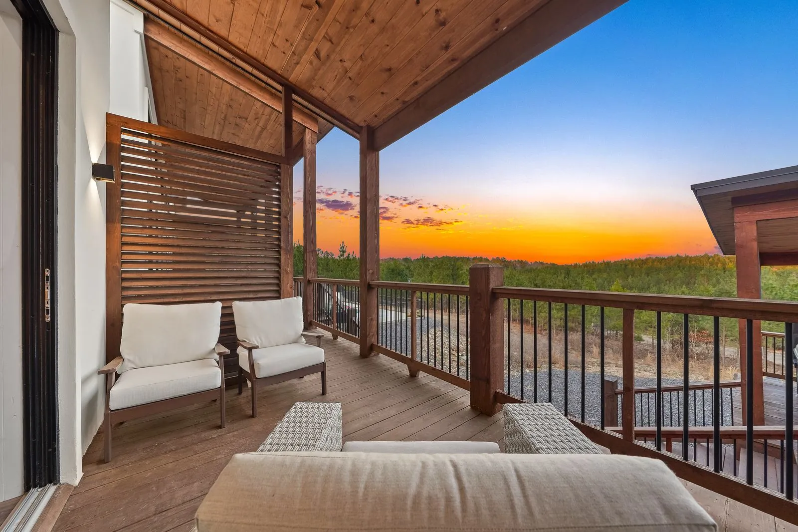 Private covered balcony off bedroom at The Malibu with white lounge chair, wood ceiling, and pine tree views