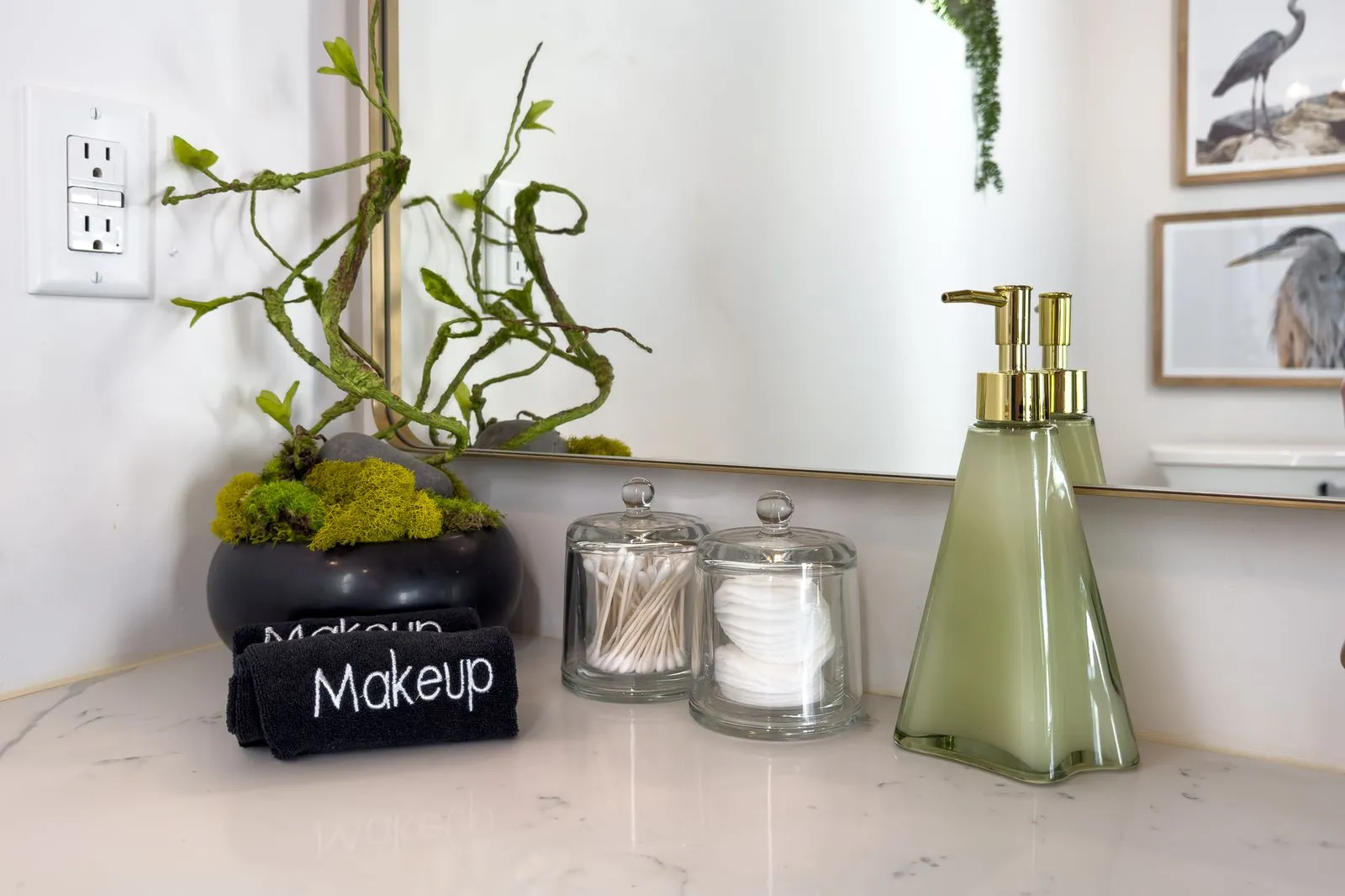 Guest amenity display at The Malibu with makeup bags, green glass soap dispensers, and decorative greenery on marble counter