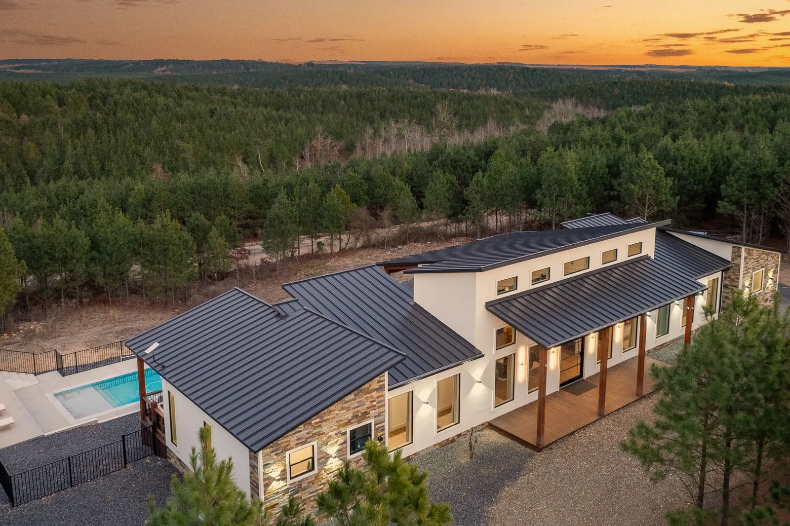 Aerial twilight view of a Haute Vie Airbnb Luxe cabin with a private pool surrounded by Broken Bow pine forest