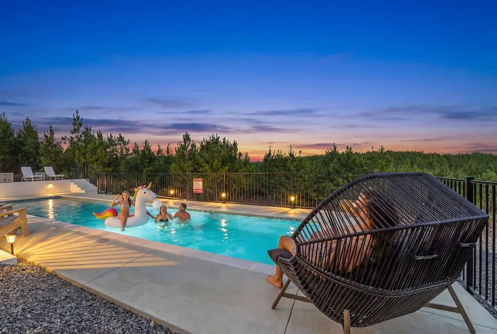 Guests relaxing in the illuminated pool with a forest backdrop at twilight