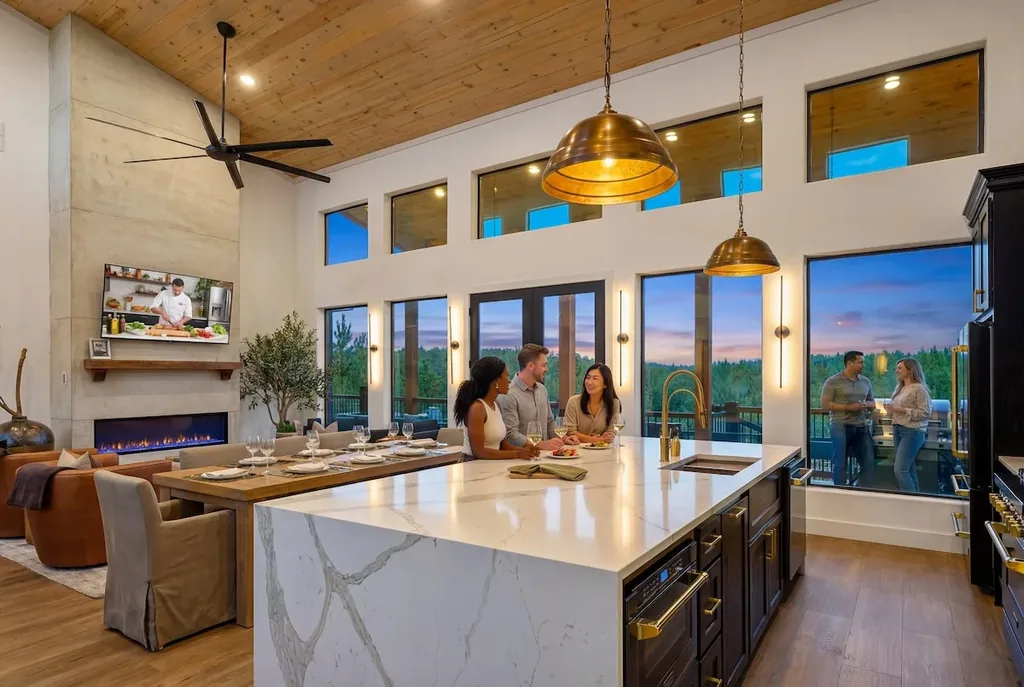 Guests around the marble kitchen island in the open great room with fireplace and sunset windows