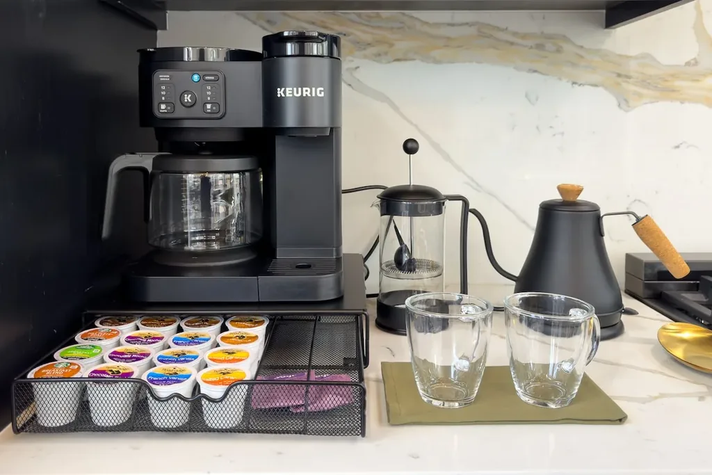 Coffee station with Keurig, kettle, pods, glasses, and marble backsplash