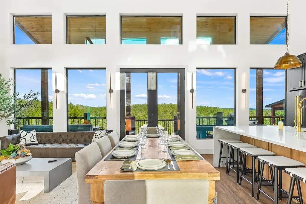 Dining table framed by tall windows with broad forest views
