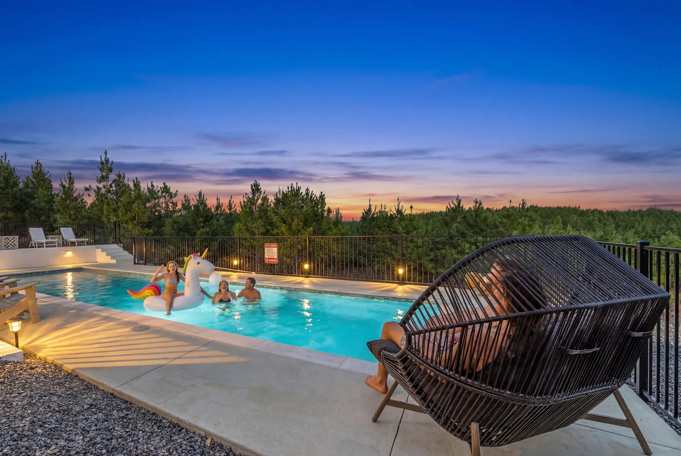 Family swimming in a private heated cabin pool at dusk surrounded by pines